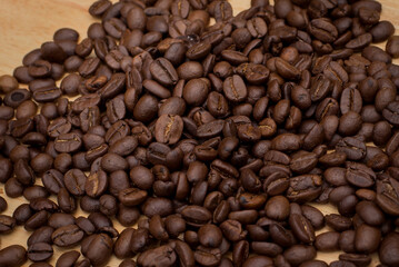 Many coffee beans placed around  in a warm on wood background.
