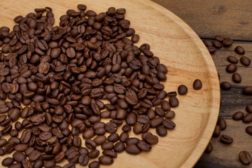 Many coffee beans placed around on a wooden dish in a warm on wood background.