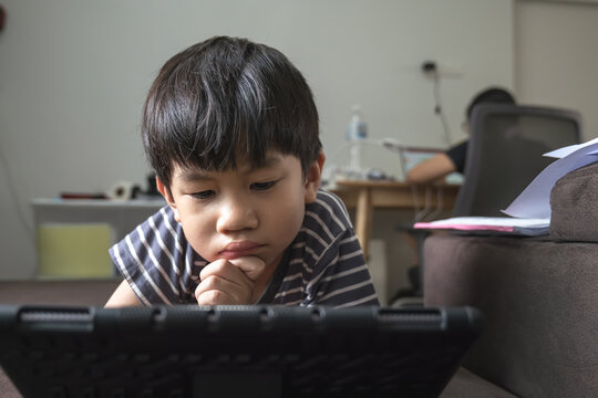Asian boy addictive watching tablet  while his mother working on the computer in the background.