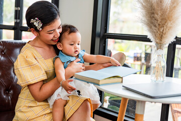 A happy Chinese Asian mother and her young daughter are interested in morning books together in the living room at home. family activity concept.