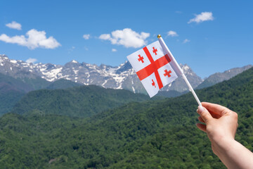 Georgian flag in woman's hand on Background of Mountains and Blue Sky.