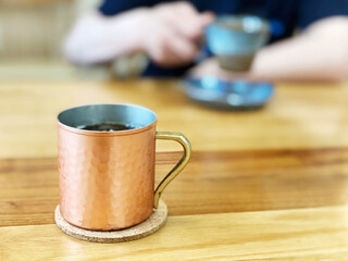 銅マグカップと向かい側でコーヒーを飲む人