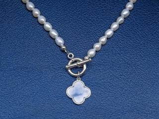 Fototapeta na wymiar Luxury elegant baroque pearl necklace with pendant on dark blue textured leather background
