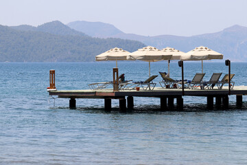 Beach holiday on sea resort, pier with lounge chairs and parasols. Scenic view to the green...