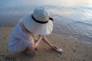 石垣島の夕日のビーチで貝殻で遊ぶ女性がいる風景 沖縄 Landscape of a woman playing with seashells on a beach at sunset in Ishigaki Island, Okinawa. 