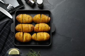 Delicious homemade Hasselback potatoes on black table, flat lay. Space for text