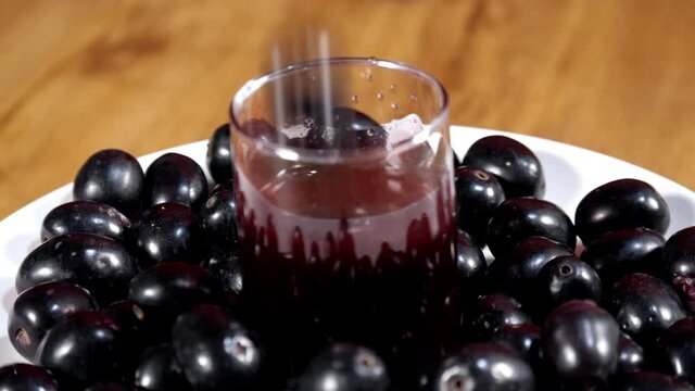 A few black Jamuns falling into a transparent glass of juice - a tasty drink. Indian summer fruit. An extreme closeup shot of Indian blackberries decorated nicely on a plate rotating on a turntable