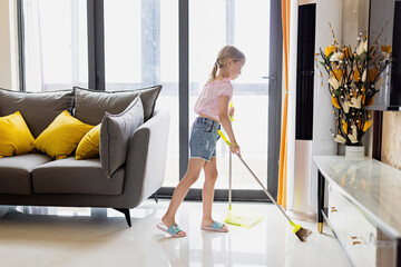 Little Caucasian blonde girl with blonde hair seven years old cleaning floor in living room. Modern home interior, domestic life.