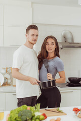 Happy couple love cooking together in kitchen. Young loving man and woman standing in the white kitchen room.