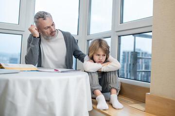 Gray-haired bearded man talking to his kid while he looking moody