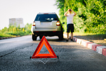 Triangle sign and person with a broken car on the road