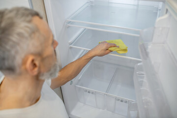 A gray-haired man cleaning the fridge in the kitchen