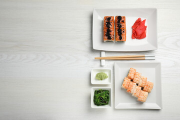 Delicious sushi rolls served on white wooden table, flat lay. Space for text