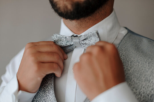 Stylish groom adjusting bow tie
