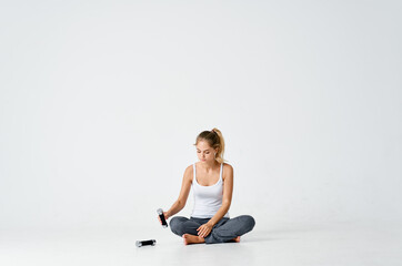 Fototapeta premium athletic woman sitting on the floor barefoot dumbbell workout light background