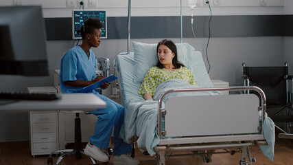 Afro-american nurse discussing with sick woman monitoring illness symptom writing healthcare...