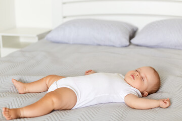 Fototapeta na wymiar Peaceful baby lying on a bed while sleeping in a soft bed on grey blanket, infant wearing white bodysuit sleeps alone indoor, childhood.