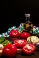 Close up of traditional summer cold tomato soup gazpacho ingredients on a wood plank -Tomatoes, pepper, cucumber, garlic and olive oil - black background - mediterranean, spanish food concept