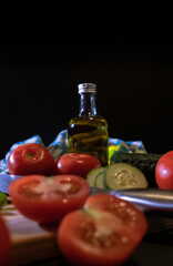 Mediterranean ingredients on a wood plank -Tomatoes, cucumbers and one bottle of olive oil - black background - Healthy, spanish food concept - selective focus