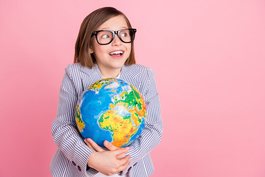 Portrait of attractive cheerful girl hugging globe looking aside copy space isolated over pink pastel color background
