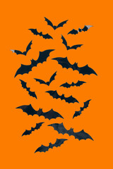 Halloween background - decorative paper bats on orange background with copy space. Halloween decorations or party invitation concept. Selective focus, vertical image