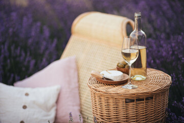 Wicker chair and table with glass of wine, fresh brie cheese and olives in lavender field.