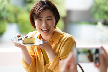 	ケーキを持ち写真を撮る女性