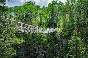 Obraz premium View from the Rimouski river on the highest suspended footbridge in Quebec, 63 meters high and 99 meters long, located in Canyon des Portes de l'Enfer (Hell's gate Canyon) in Quebec, Canada