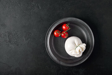 Italian burrata cheese and branch of cherry tomatoes on dark plate. Top view, copy space