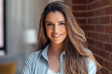 Smiling young woman looking at camera while standing in the living room at home.