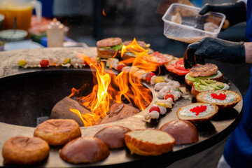 Chef preparing shrimp, prawn skewers and burgers with red caviar, avocado on brazier with hot flame at summer local food market - close up. Outdoor cooking, seafood, gastronomy, street food concept - obrazy, fototapety, plakaty