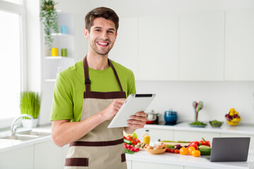Photo portrait young man in apron keeping tablet smiling in the kitchen