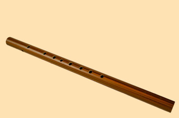 Brown bamboo flute instrument isolated on a soft yellow background.