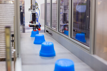 Blue polypropylene pots on conveyor belt of automatic plastic injection molding machine with...