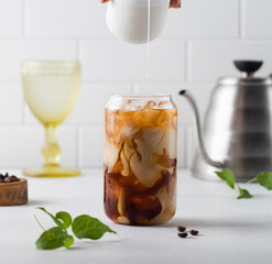 Cream is poured into cold black coffee with ice cubes. Coldbrew. Summer drinks.