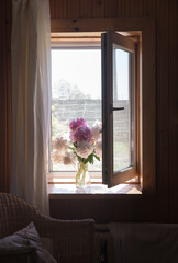 bouquet on the window close-up. a light breeze ruffles the tulle on the old window. there is a vase with peonies on the window. the interior of a rural house. the concept of comfort and relaxation