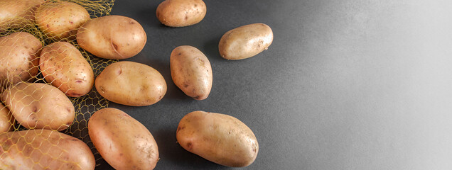 Obraz premium unpeeled raw potatoes scattered on grey table. Plastic mesh sack