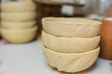 Close up view - stack of unfinished clay plates on shelf of pottery workshop, ceramic studio. Crafting, DIY, handmade, small business, traditional, manufacturing, art concept