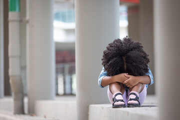 The afro curly haired girl bend down the head sit down alone at under building.mental health...