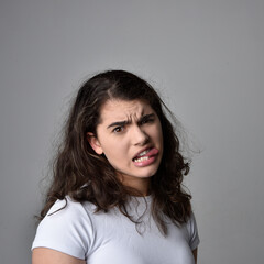 Fototapeta premium Close up portrait of young woman with natural brown hair, over the top facial expressions on light grey studio background.