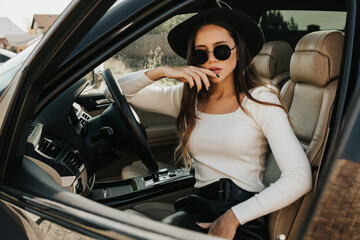 Plakat Portrait of a beautiful young woman driving a car. Lady in blackout glasses posing in the car