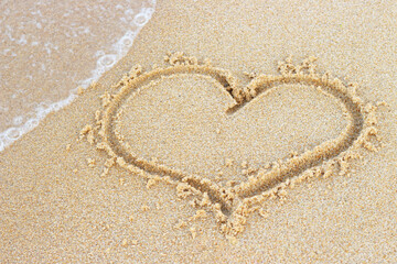 A heart shape drawn on sand on the beach close-up.
