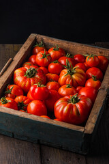 Ripe tomatoes in a wooden box.  Fresh vegetables on a black wooden background. 