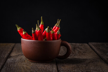 Red chili peppers in a clay chashketna dark background.
