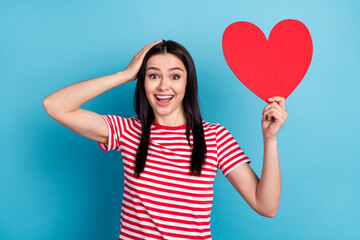 Photo of young girl amazed excited surprised happy smile hold paper heart valentine day isolated over blue color background