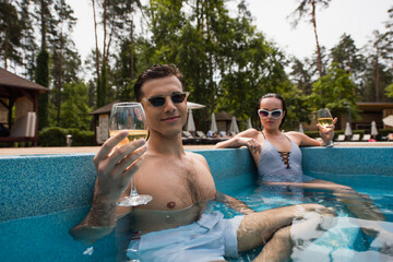 Man holding glass of wine near blurred girlfriend in pool