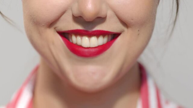 Lips with red lipstick close-up. Caucasian brunette girl smiling wide showing teeth. Anonymous lady studio still shot slow motion.