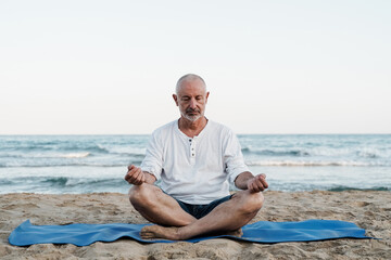 Senior man doing yoga meditation outdoor at the beach - Elderly and healthy lifestyle - Focus on...