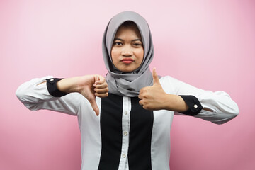 Beautiful asian young muslim woman with hand sign like or dislike, yes or no, happy or sad, comparing two things, isolated on pink background