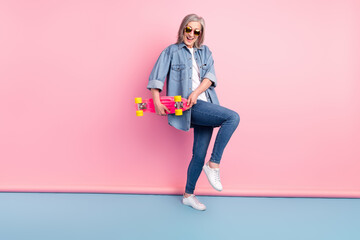Full length photo of charming old funky woman hold hands longboard feel young isolated on pink color background